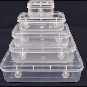May include: Five clear plastic storage boxes of different sizes, stacked. Each box has a rectangular shape, a hinged lid, and a secure latch. The boxes are arranged in a pyramid, with the largest at the base. The boxes are made of clear plastic.
