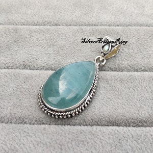 May include: A teardrop-shaped pendant with a light blue aquamarine gemstone set in a silver bezel with a beaded border. The pendant has a silver bail with a decorative design.