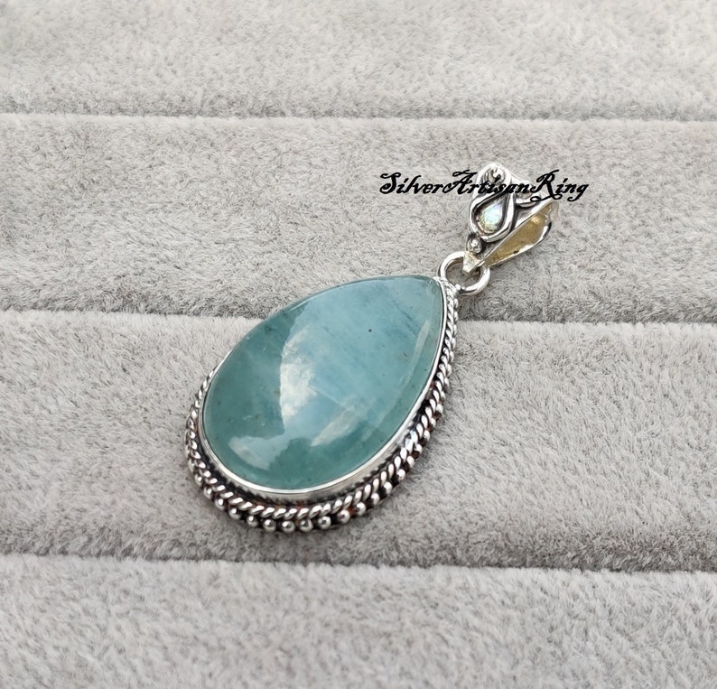 May include: A teardrop-shaped pendant with a light blue aquamarine gemstone set in a silver bezel with a beaded border. The pendant has a silver bail with a decorative design.