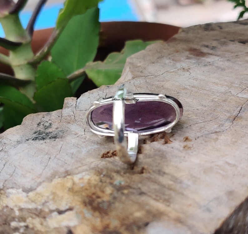 May include: A silver ring with a large oval amethyst gemstone. The ring is set in a simple band and the stone is faceted.