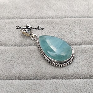 May include: A teardrop-shaped pendant with a light blue aquamarine gemstone set in a silver bezel with a detailed silver bail.