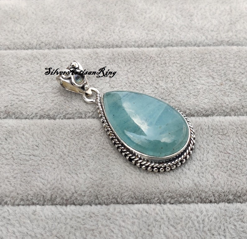 May include: A teardrop-shaped pendant with a light blue aquamarine gemstone set in a silver bezel with a detailed silver bail.