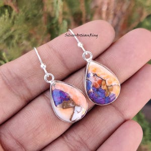 Pu&ograve; includere: Un paio di orecchini pendenti in argento sterling con gocce di pietre preziose a forma di lacrima di colore viola, arancione e bianco.