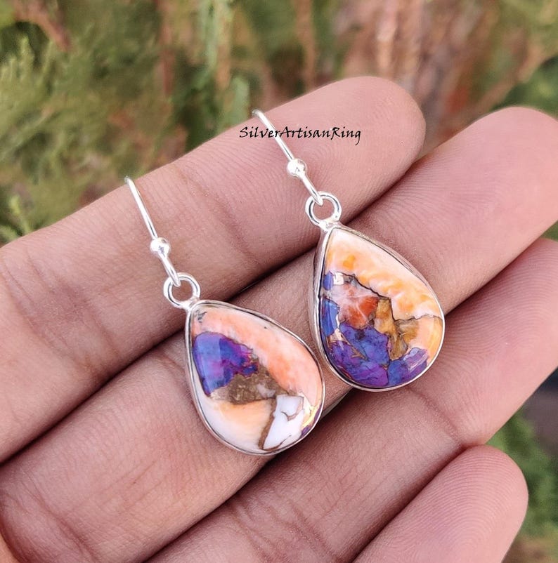 Pu&ograve; includere: Un paio di orecchini pendenti in argento sterling con gocce di pietre preziose a forma di lacrima di colore viola, arancione e bianco.
