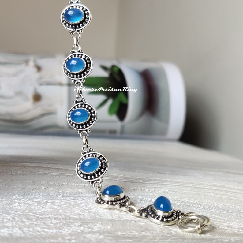 May include: A silver bracelet with blue gemstone accents. The bracelet has a lobster claw clasp.