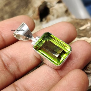 Pode incluir: Um pingente retangular de pedra preciosa verde lim&atilde;o com moldura de prata. O pingente tem um corte retangular e &eacute; colocado em uma moldura de prata polida. O pingente &eacute; segurado em uma m&atilde;o.