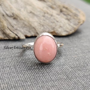May include: A silver ring featuring a pink oval opal gemstone. The ring is set in a simple, bezel setting.