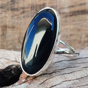 Puede incluir: Un anillo de plata con una gran piedra ovalada de ónix negro. El anillo está engastado en un estilo simple y elegante.