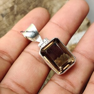 Pode incluir: Um pingente de prata com uma pedra preciosa marrom. A pedra preciosa &eacute; cortada em forma de esmeralda e tem um acabamento facetado. O pingente est&aacute; em uma corrente de prata.