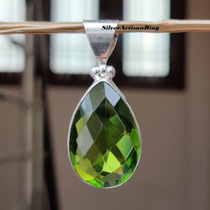 May include: A silver pendant with a teardrop-shaped green gemstone. The gemstone is faceted and has a high shine.