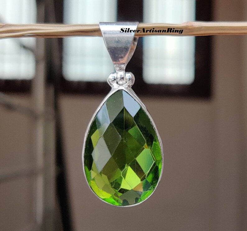 May include: A silver pendant with a teardrop-shaped green gemstone. The gemstone is faceted and has a high shine.