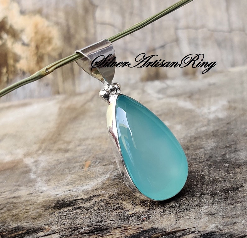May include: A teardrop-shaped pendant featuring a light blue chalcedony stone set in sterling silver. The pendant has a bail for attaching to a chain.