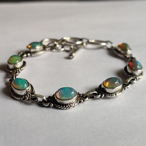 May include: A silver bracelet with a chain link design and oval-shaped opal stones. The stones are iridescent with shades of green, blue, and orange.