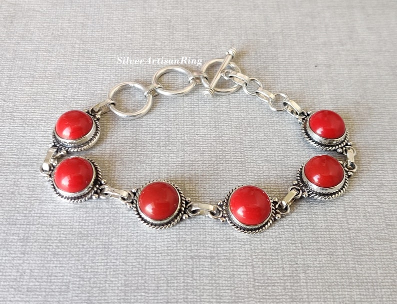 May include: A silver bracelet with a toggle clasp and five red gemstone cabochons. The bracelet has a delicate chain design.