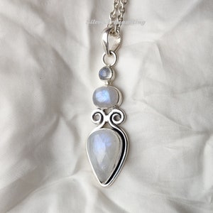 May include: A silver pendant necklace with a teardrop-shaped moonstone and two round moonstones. The pendant is set in a silver frame with a decorative design.