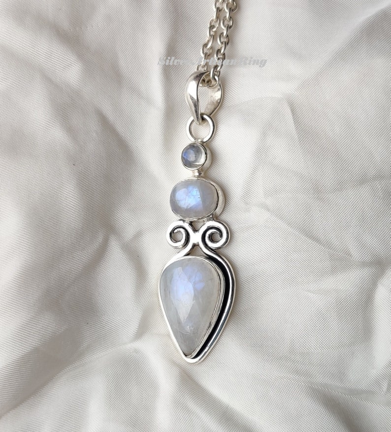 May include: A silver pendant necklace with a teardrop-shaped moonstone and two round moonstones. The pendant is set in a silver frame with a decorative design.