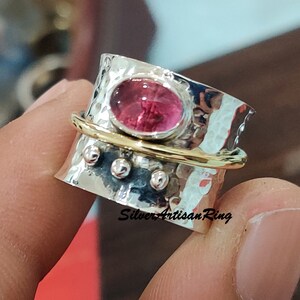 Könnte beinhalten: Ein silberner Ring mit einem rosafarbenen Edelstein, der in eine gehämmerte Band gefasst ist. Der Ring hat eine goldene Band um die Mitte und drei silberne Perlen an der Seite.