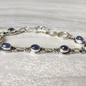May include: A silver bracelet with a chain link design and oval-shaped blue gemstones. The bracelet has a clasp closure.