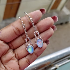 May include: A pair of silver dangle earrings with iridescent oval opal stones. The earrings have a delicate, knotted design.