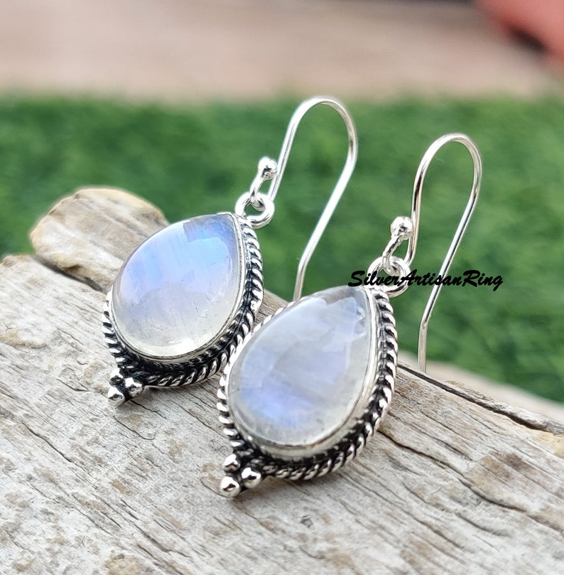 May include: A pair of silver dangle earrings with teardrop-shaped moonstone gemstones. The earrings have a delicate, intricate design with a twisted rope border and small silver beads.