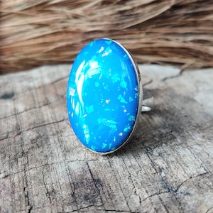 Könnte beinhalten: Ein silberner Ring mit einem blauen, ovalen Opal-Edelstein. Der Opal hat eine glitzernde, irisierende Oberfläche.