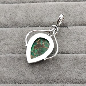 May include: A silver pendant with a green and brown pear-shaped stone set in a silver bezel. The pendant is on a silver chain.