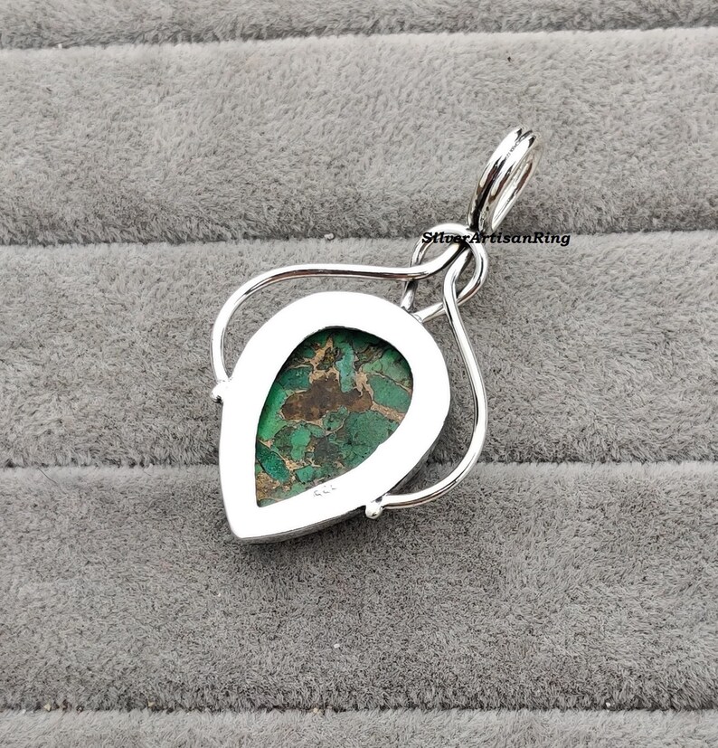 May include: A silver pendant with a green and brown pear-shaped stone set in a silver bezel. The pendant is on a silver chain.