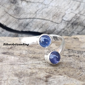 Könnte beinhalten: Ein silberner Ring mit zwei blauen Edelsteinen, die in die Band eingefasst sind. Der Ring ist verdreht und hat ein einzigartiges Design.