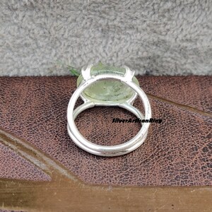 May include: A silver ring with a green gemstone set in a bezel setting. The ring is on a brown leather surface.
