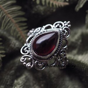 May include: A silver ring with a teardrop-shaped red gemstone set in a filigree design.