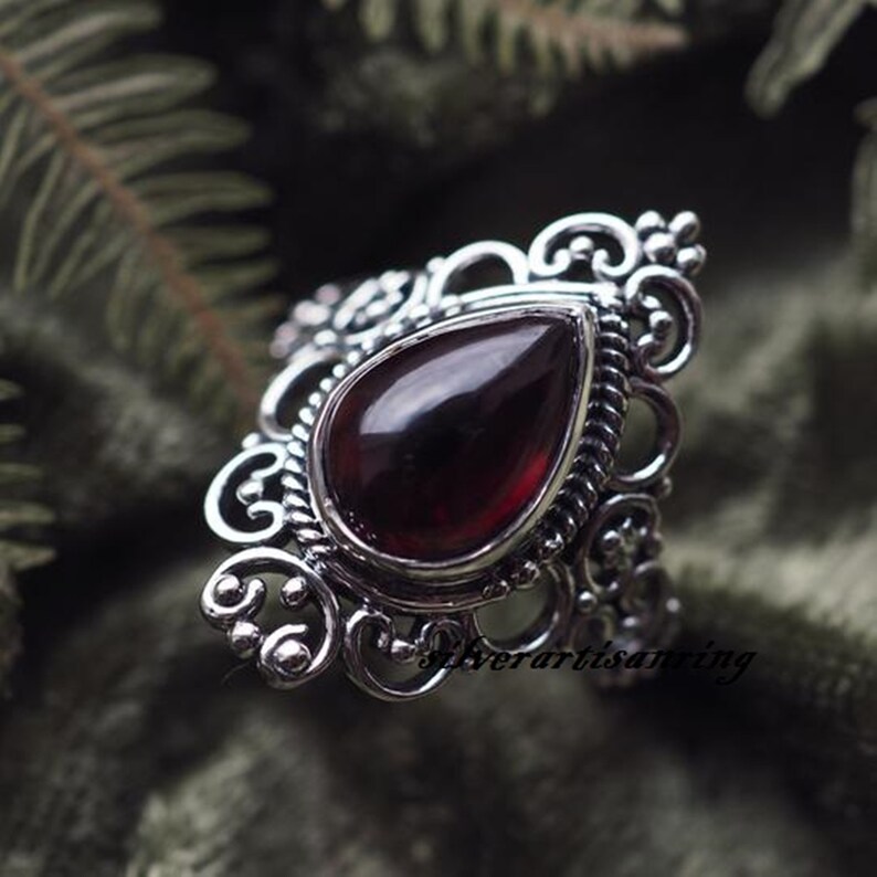 May include: A silver ring with a teardrop-shaped red gemstone set in a filigree design.
