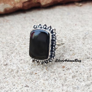 Könnte beinhalten: Rechteckiger Ring aus schwarzem Onyx mit einer silberfarbenen, strukturierten Fassung. Der Ring hat einen perlenbesetzten Rand um den schwarzen Stein. Der Text "SilverArtisanRing" ist sichtbar.