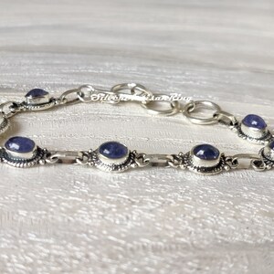 May include: A silver bracelet with a chain link design and oval-shaped blue gemstones. The bracelet has a clasp closure.