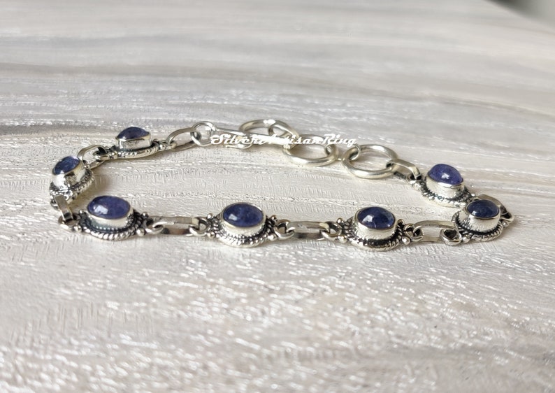 May include: A silver bracelet with a chain link design and oval-shaped blue gemstones. The bracelet has a clasp closure.