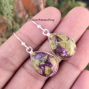 Pu&ograve; includere: Un paio di orecchini pendenti in argento con gocce di pietre preziose verdi e viola. Gli orecchini hanno una forma a goccia e sono realizzati in argento sterling.