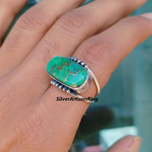 Könnte beinhalten: Ein silberner Ring mit einem rechteckigen, türkisfarbenen Stein. Der Stein hat eine einzigartige, strukturierte Oberfläche mit goldfarbenen Akzenten. Der Text "SilverArtisanRing" ist sichtbar. Ein Schmuckstück.