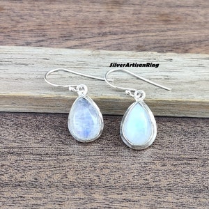 Könnte beinhalten: Ein Paar silberne Tropfenohrringe mit Mondstein-Edelsteinen. Die Ohrringe haben ein schlichtes Design und sind perfekt für den Alltag.