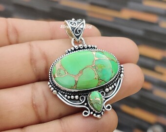 May include: A silver pendant featuring a large oval green turquoise stone with brown veins and a smaller teardrop-shaped green turquoise stone. The pendant has intricate silver detailing.