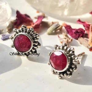 Könnte beinhalten: Ein Paar silberne Ohrringe mit einem roten Rubin-Edelstein, der in einem Sternburst-Design gefasst ist.