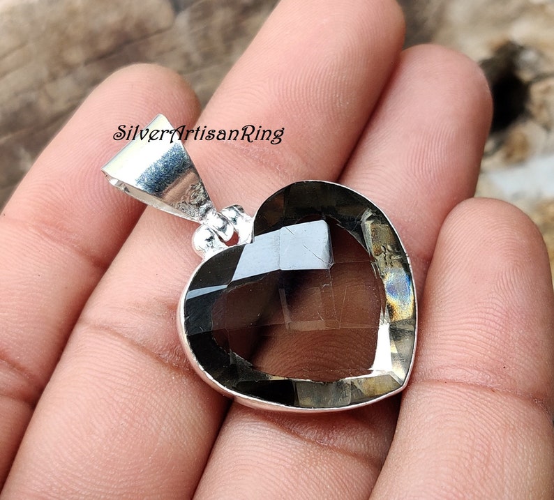 May include: A silver heart-shaped pendant with a smoky quartz gemstone. The pendant has a bail for attaching to a chain.