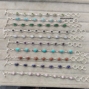 Puede incluir: Nueve pulseras de plata con piedras preciosas de diferentes colores. Cada pulsera tiene un cierre de palanca y una extensión de cadena. Las piedras preciosas incluyen verde, turquesa, negro, blanco, amatista, rojo, azul y rosa.