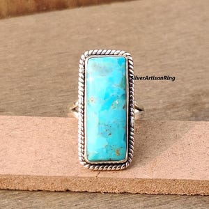 Könnte beinhalten: Ein türkisfarbener Ring mit einem silbernen Band und einem rechteckigen Türkis-Stein. Der Stein hat eine blaue und grüne Farbe mit einem marmorierten Muster. Das Band hat ein seilartiges Design.