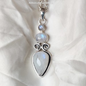 May include: A silver pendant necklace with three moonstone gems. The pendant features a teardrop-shaped moonstone, a round moonstone, and a smaller round moonstone.