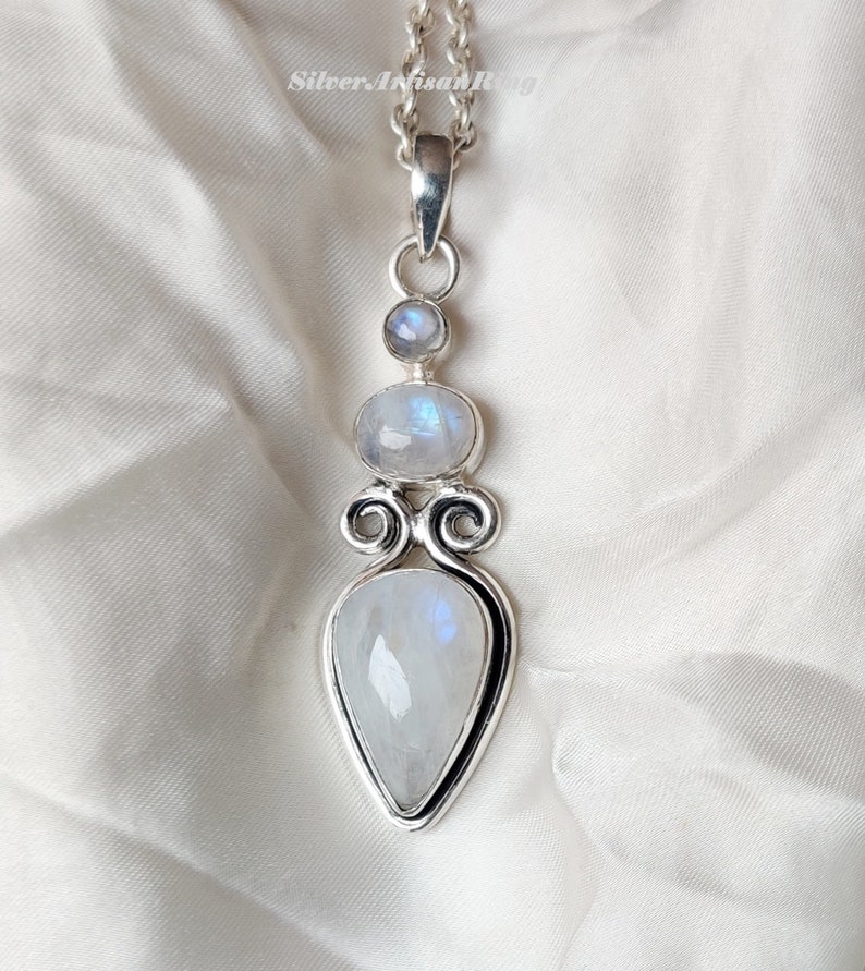 May include: A silver pendant necklace with three moonstone gems. The pendant features a teardrop-shaped moonstone, a round moonstone, and a smaller round moonstone.