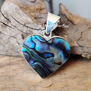 May include: A silver heart-shaped pendant with a blue and green abalone shell inlay. The pendant is on a wooden surface.