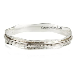 以下が含まれることがあります： ハンマー仕上げとビーズエッジが付いたシルバーのバングルブレスレット。このブレスレットはSilverArtisanRingによって作られています。