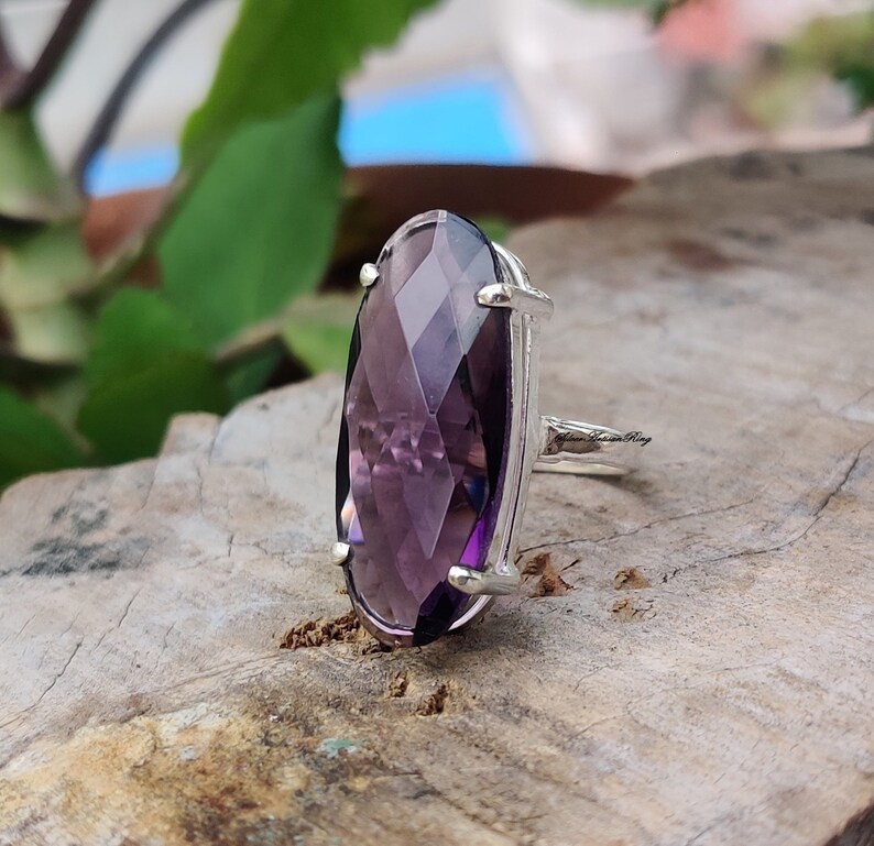 May include: A silver ring with a large, faceted, oval-shaped amethyst gemstone. The ring is set in a simple, elegant design.
