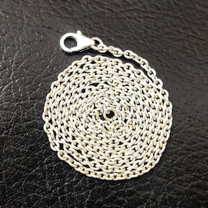 Könnte beinhalten: Eine silberne Kettenkette mit einem Karabinerverschluss. Die Kette ist zu einem Kreis gewickelt.
