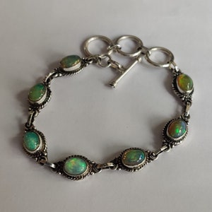 May include: A silver bracelet with a toggle clasp features six oval-shaped green opals.