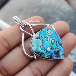 May include: A silver pendant featuring a teardrop-shaped abalone shell with iridescent blue, green, and purple hues. The shell is set in a silver frame with a twisted bail.